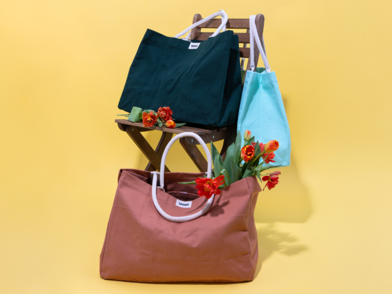 Un sac cabas rose poudré, un sac cabas turquoise menthe et un sac cabas bleu indigo sur une chaise avec des fleurs - Grand Beau